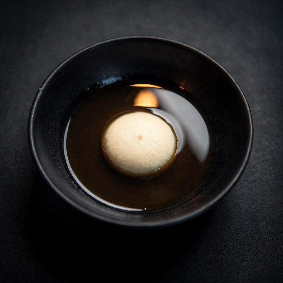 Dark allium broth held around a quiet pale center.