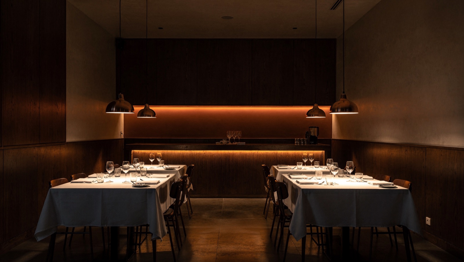 Empty dining room between services under low copper pendant lamps.