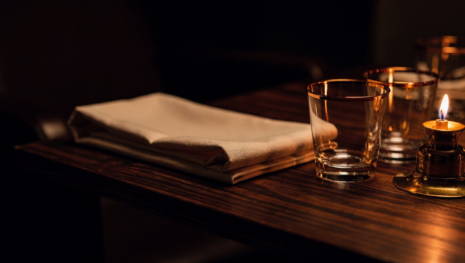 Folded linen, two glasses and a single small flame at a reserved table corner.